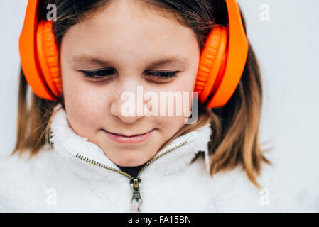 Fille de l'école primaire avec des cheveux blonds en blanc manteau de fourrure de zippés avec orange vif des écouteurs Banque D'Images