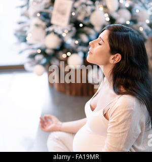 Femmes enceintes en bonne santé faisant de l'exercice de yoga à Noël avec les yeux fermés, assis en lotus poser et méditer Banque D'Images