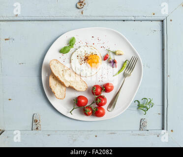 Le petit-déjeuner ensemble. Les tranches de pain frit, oeuf, tomates cerises, poivrons et les herbes sur une plaque en céramique blanc bleu clair au bac en bois Banque D'Images