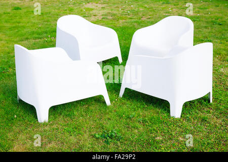 Quatre chaises en plastique blanc moderne, debout sur l'herbe verte fraîche Banque D'Images