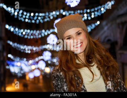 Ce Noël est l'écrasement sur la mode de l'avant les courses. Portrait of smiling young woman standing dans la face de lumière de Noël Banque D'Images