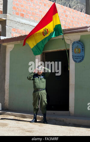 Un policier ajuste son chapeau sous un drapeau bolivien en face du poste de police à Luribay, Bolivie, Amérique du Sud Banque D'Images