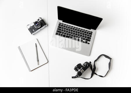 Vue de dessus de deux caméras, le bloc-notes avec stylo et un écran blanc ordinateur portable isolé sur fond blanc Banque D'Images