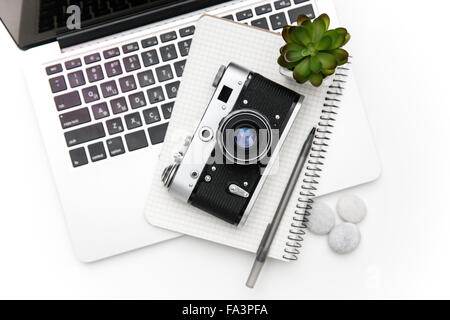 Vue de dessus de l'ordinateur portable et le bloc-notes avec pan couché au vintage ancien appareil photo et vert flover over white background Banque D'Images