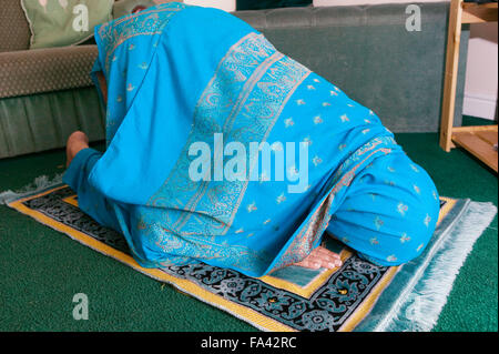 Femme musulmane à genoux sur le sol en récitant des prières islamiques à la maison, Banque D'Images