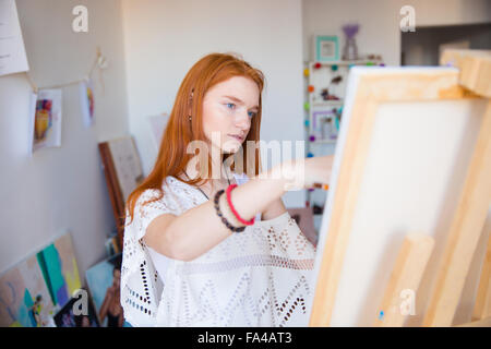 Belle pensive young woman painter avec longs cheveux rouges travaillant dans art studio Banque D'Images