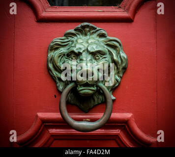 Une tête de lion avec un anneau dans sa bouche est un doorknocker sur une porte en bois rouge. Banque D'Images