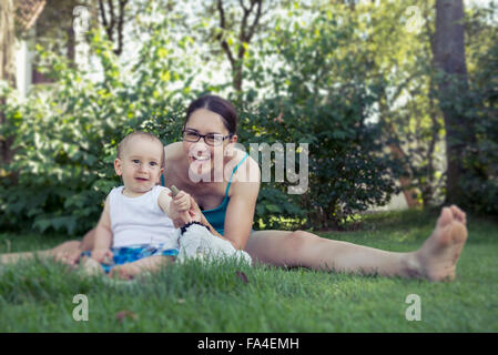 Bébé garçon et sa mère jouant avec des cailloux dans la pelouse et souriant, Munich, Bavière, Allemagne Banque D'Images