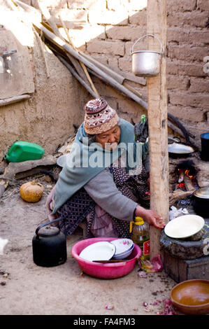 De soleil femme bolivienne portant un chapeau en laine tricoté et la cuisson de la terre-de-chaussée cuisine dans un village de Bolivie Banque D'Images