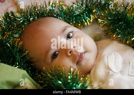 Un petit bébé couché dans un lit avec une guirlande de noël Banque D'Images