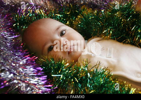 Très peu cute girl lying in bed with a Christmas garland Banque D'Images