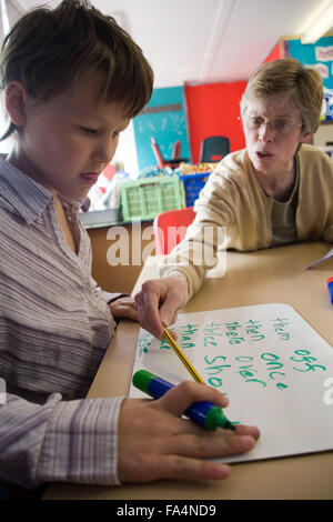 Girl sitting in classroom la pratique de l'écriture ; avec l'aide de l'enseignant, Banque D'Images