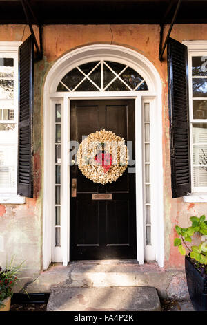 Porte à un accueil traditionnel le long de la rue de l'église décorée d'une couronne de Noël pour la saison de vacances à Charleston, SC. Banque D'Images