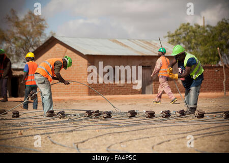 Chaîne de travailleurs nouveaux câbles d'alimentation dans un village rural près de Dodoma, Tanzanie, Afrique de l'Est. Banque D'Images