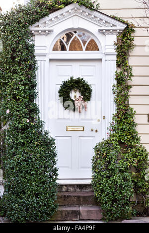 Porte à un accueil traditionnel le long de la rue de l'église décorée d'une couronne de Noël pour la période des fêtes dans le quartier historique de Charleston, SC. Banque D'Images