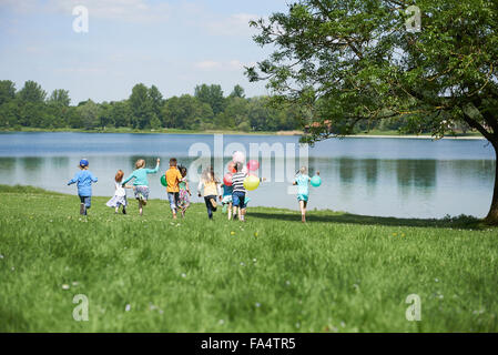 Vue arrière d'enfants courant dans le parc avec des ballons, lac Karlsfeld, Munich, Bavière, Allemagne Banque D'Images