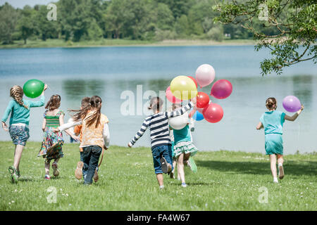 Vue arrière d'enfants courant dans parc avec des ballons, Munich, Bavière, Allemagne Banque D'Images