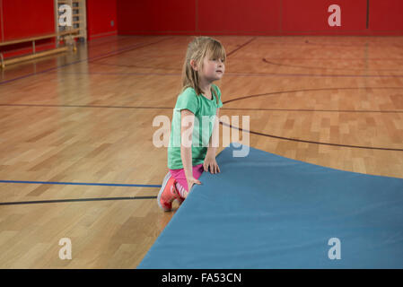 Fille d'essayer de soulever les tapis d'exercice dans la région de basket-ball de sports hall, Munich, Bavière, Allemagne Banque D'Images