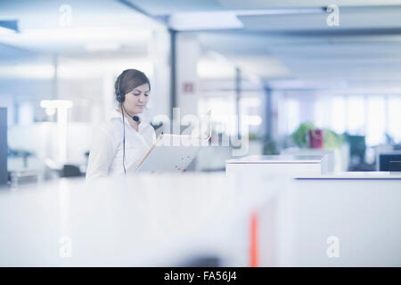 Femme d'affaires portant un casque et un document de lecture dans le cubicle, Freiburg Im Breisgau, Bade-Württemberg, Allemagne Banque D'Images