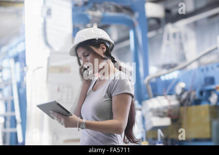 Ingénieur femelle à l'aide d'une tablette numérique et le téléphone mobile dans une installation industrielle, Bade-Wurtemberg, Allemagne Banque D'Images
