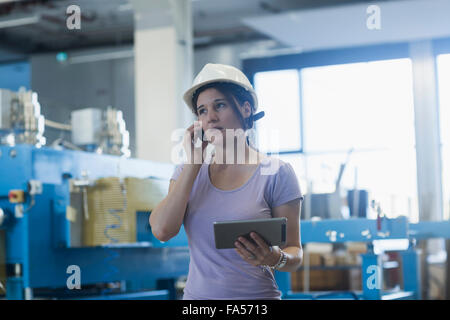 Ingénieur femelle à l'aide d'une tablette numérique et le téléphone mobile dans une installation industrielle, Bade-Wurtemberg, Allemagne Banque D'Images