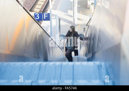 Jeune femme déménagement sur l'escalator et parlant au téléphone à la gare de Freiburg im Breisgau, Bade-Wurtemberg, Allemagne Banque D'Images