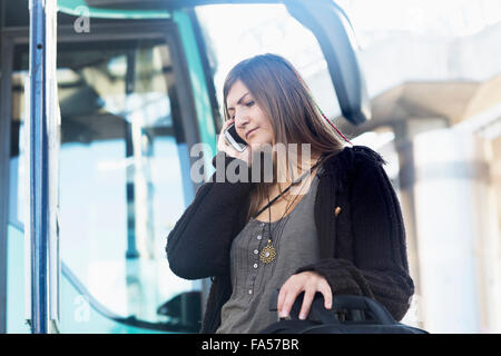 Young Woman talking on mobile phone et debout devant des bus, Freiburg im Breisgau, Bade-Wurtemberg, Allemagne Banque D'Images