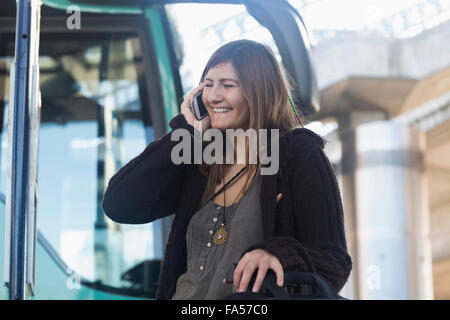 Young Woman talking on mobile phone et debout devant des bus, Freiburg im Breisgau, Bade-Wurtemberg, Allemagne Banque D'Images