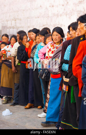 Les tibétains en vêtements traditionnels queuing contre mur blanc pour entrer dans le temple du Jokhang Banque D'Images