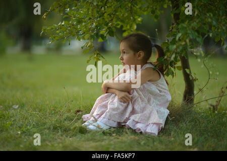 Little girl sitting under tree Banque D'Images