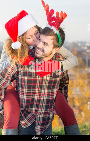 Couple in love piggyback équitation en plein air avec des chapeaux de Noël Banque D'Images