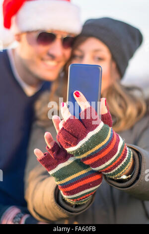 Couple wearing Christmas hats prenant un extérieur selfies Banque D'Images