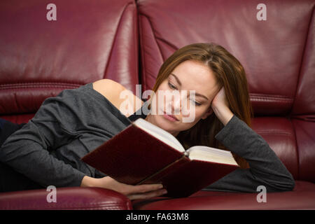 Jolie jeune femme sereine reposant sur un canapé et lire un livre à la maison Banque D'Images