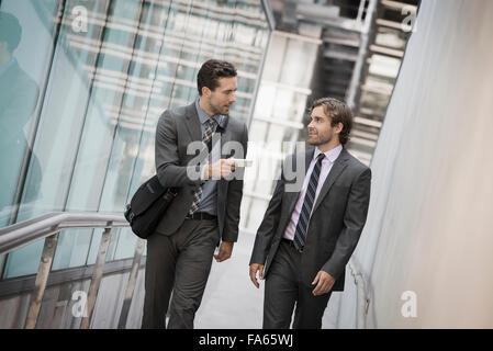 Deux hommes en costumes d'affaires à l'extérieur d'un grand bâtiment, l'un tenant un téléphone intelligent. Banque D'Images