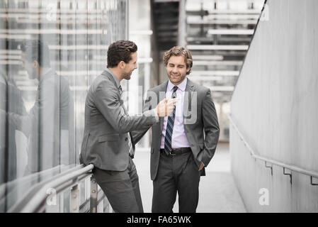 Deux hommes en costumes d'affaires à l'extérieur d'un grand bâtiment, l'un tenant un téléphone intelligent. Banque D'Images