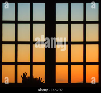 Silhouette d'une jeune fille à la recherche d'une fenêtre au coucher du soleil Banque D'Images