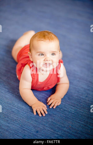 Portrait of a smiling baby girl lying on floor Banque D'Images