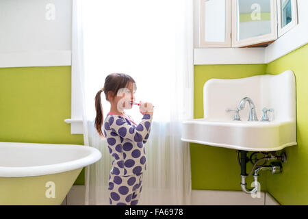 Vue de côté de fille se brosser les dents dans la salle de bains Banque D'Images
