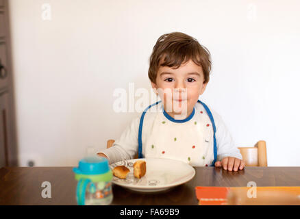 Cheeky Boy sitting at table eating snack Banque D'Images