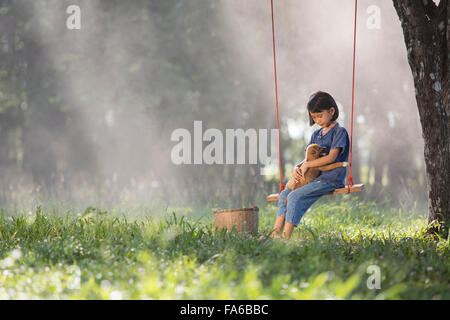 Fille assise sur une balançoire avec chien sur ses genoux Banque D'Images