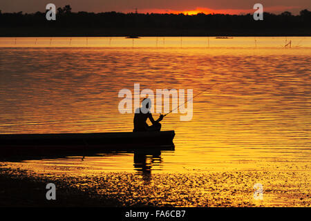 Silhouette homme assis sur un bateau de pêche au coucher du soleil Banque D'Images