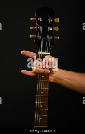 Homme hand holding manche de guitare avec des cornes de diable rock metal sign isolé sur fond noir Banque D'Images