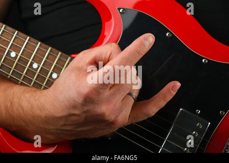 Homme hand holding red sg guitare sous le cou avec des cornes de diable rock metal sign isolé sur fond noir Banque D'Images