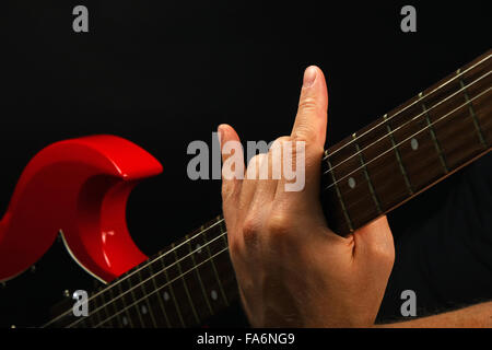 Homme hand holding red sg manche de guitare avec des cornes de diable rock metal sign isolé sur fond noir Banque D'Images