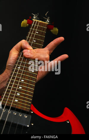 Homme hand holding red sg manche de guitare avec des cornes de diable rock metal sign isolé sur fond noir Banque D'Images