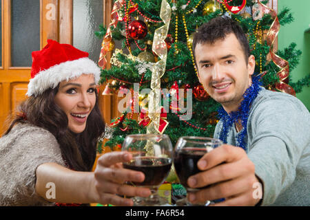 Couple à Noël à toast avec verres de vin , smiling Young man and woman in Santa's hat célébrant le Nouvel An hol Banque D'Images