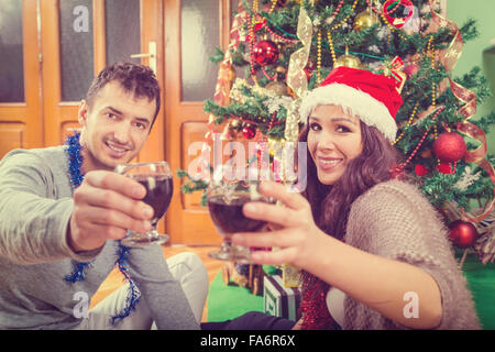 Jeune couple célébrer Noël à la maison à élever verres de vin en souriant , deux gens heureux à côté d'arbre de Noël et d'autres nouveaux Oui Banque D'Images