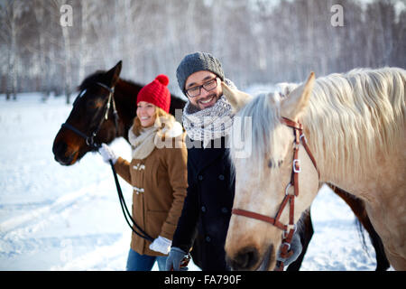 Jeune couple en train de marcher avec leurs chevaux dans le parc Banque D'Images