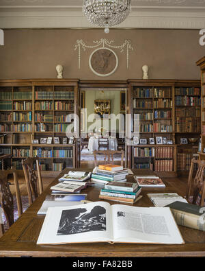 Les livres qui peuvent être consultés par les visiteurs sont disposés sur une table dans la bibliothèque de Killerton, Devon. Cette chambre a été transformée en bibliothèque au cours de l'époque édouardienne, et la salle à manger peut être vu à travers les portes ouvertes. Banque D'Images