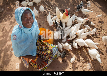 Un agriculteur nourrit ses poules en dehors de sa grange en Tengréla, village du Burkina Faso. Banque D'Images